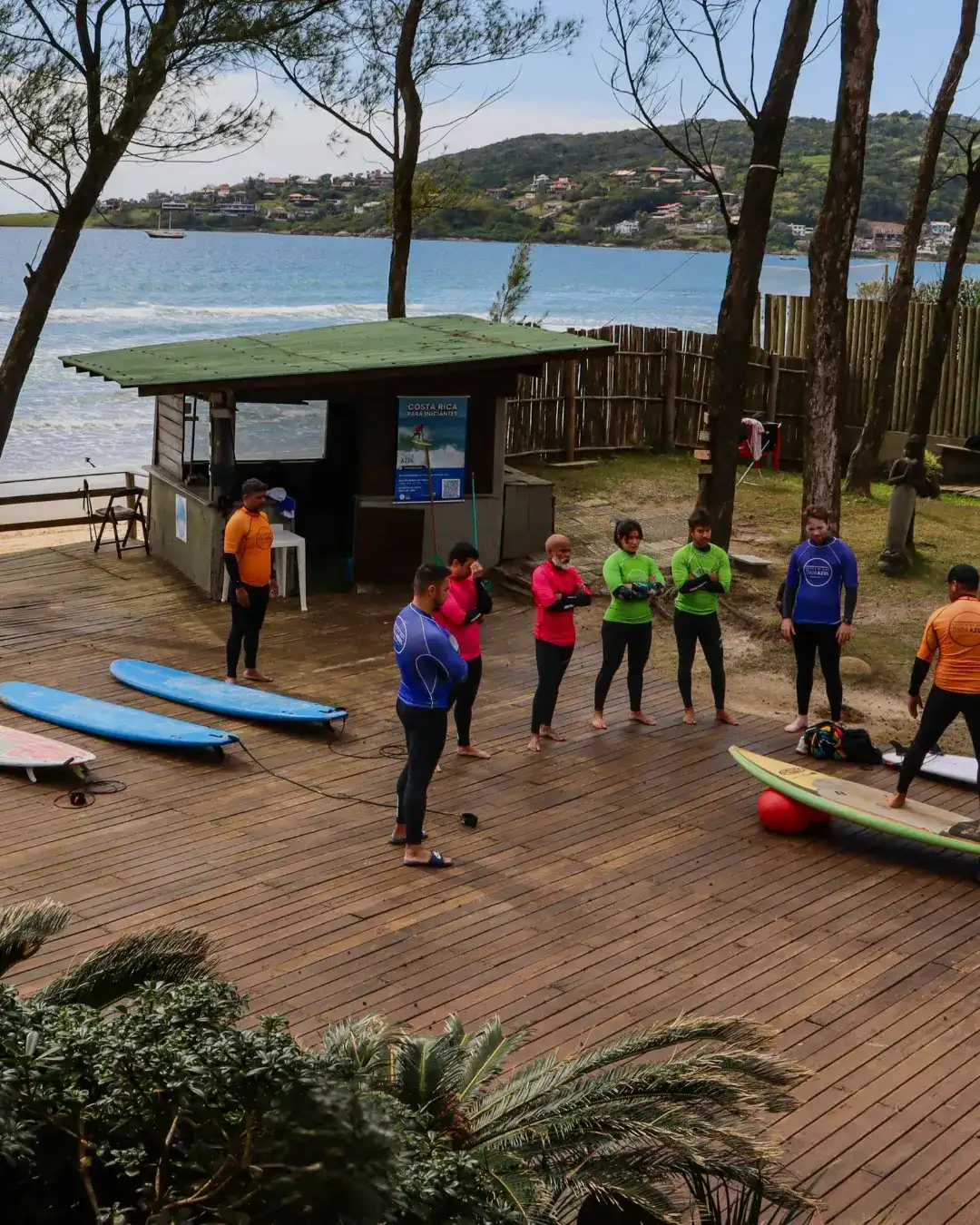 Turma de iniciantes na aula em terra, num deck de frente para o mar, antes de entrar na água