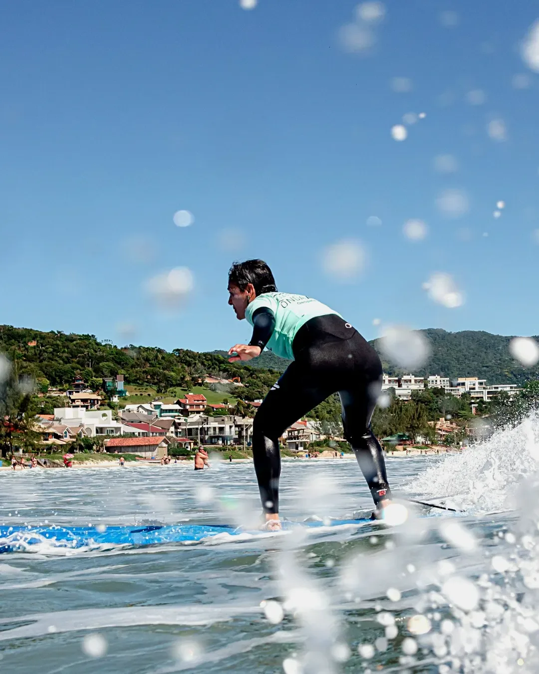 Aluno iniciante surfando com a cidade de Garopaba ao fundo